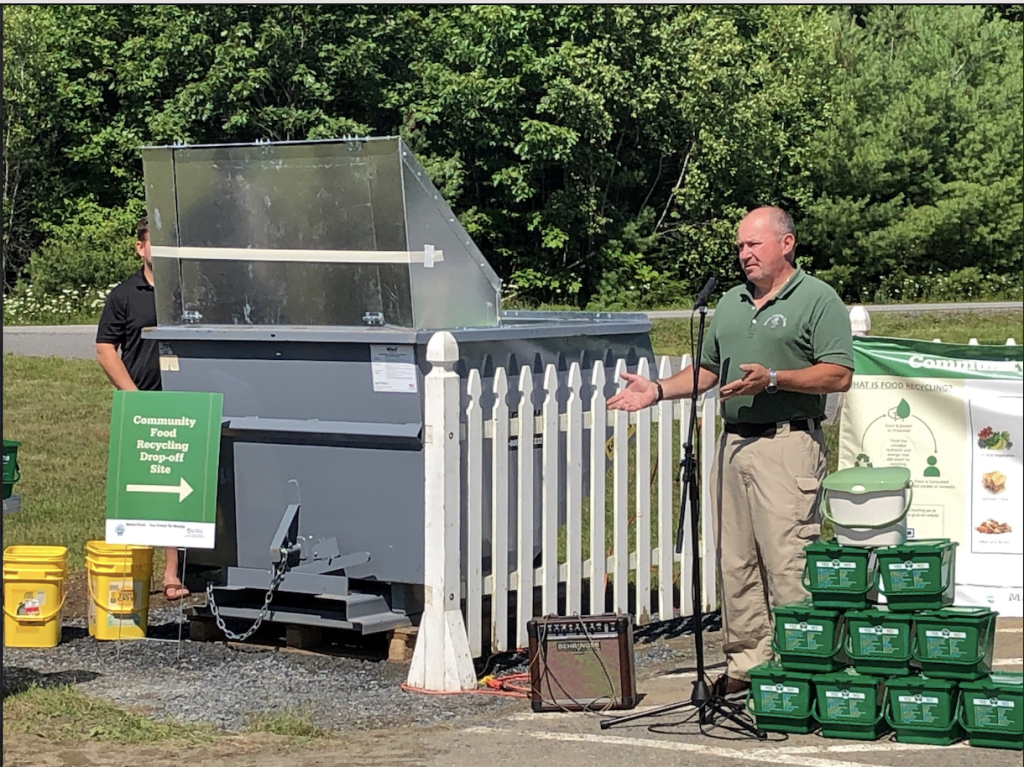 A man at the microphone next to a pile of compost buckets